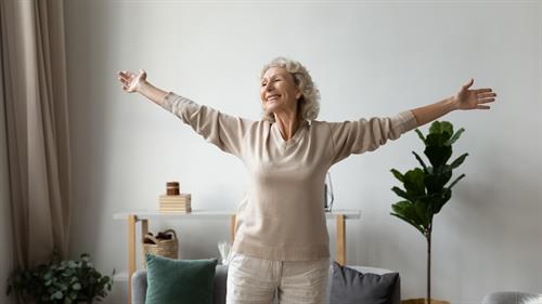 Bildet viser en eldre kvinne som strekker ut armene sine og smiler.
