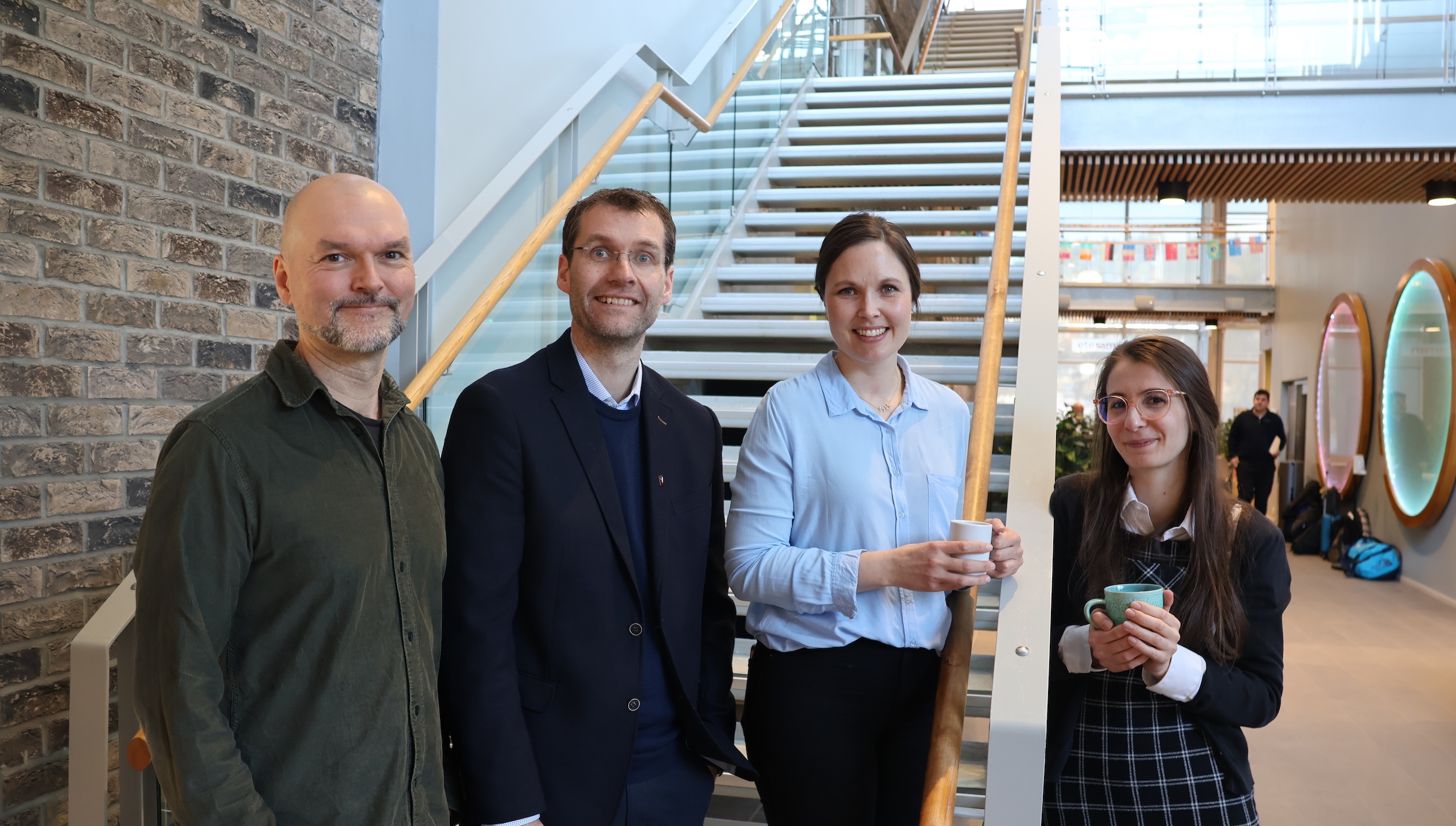 Fire personar står oppstilt i ei trapp og smiler mot kamera