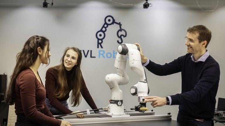 Tre mennesker som står rundt et bord og ser på en robot.