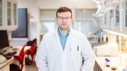 Mann i hvit frakk inne på en lab. Ser direkte inn i kameraet med armene i kors. 