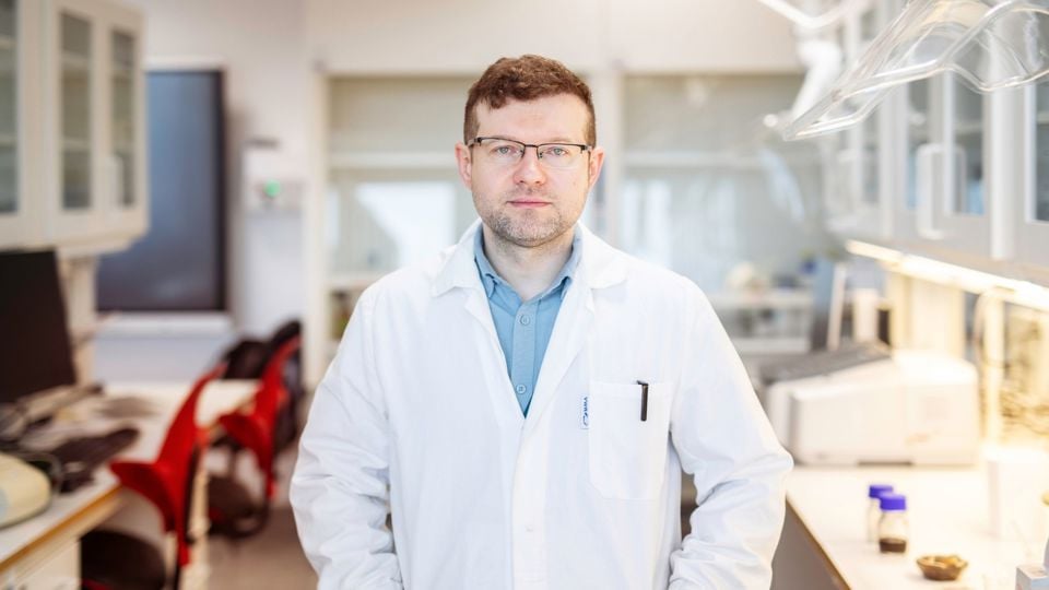 Mann i hvit frakk inne på en lab. Ser direkte inn i kameraet med armene i kors. 