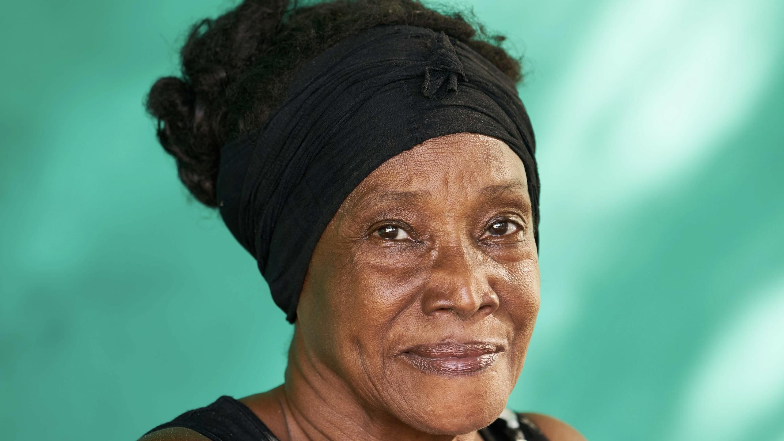 Eldre cubansk kvinne ser inn i kamera. Grønn bakgrunn