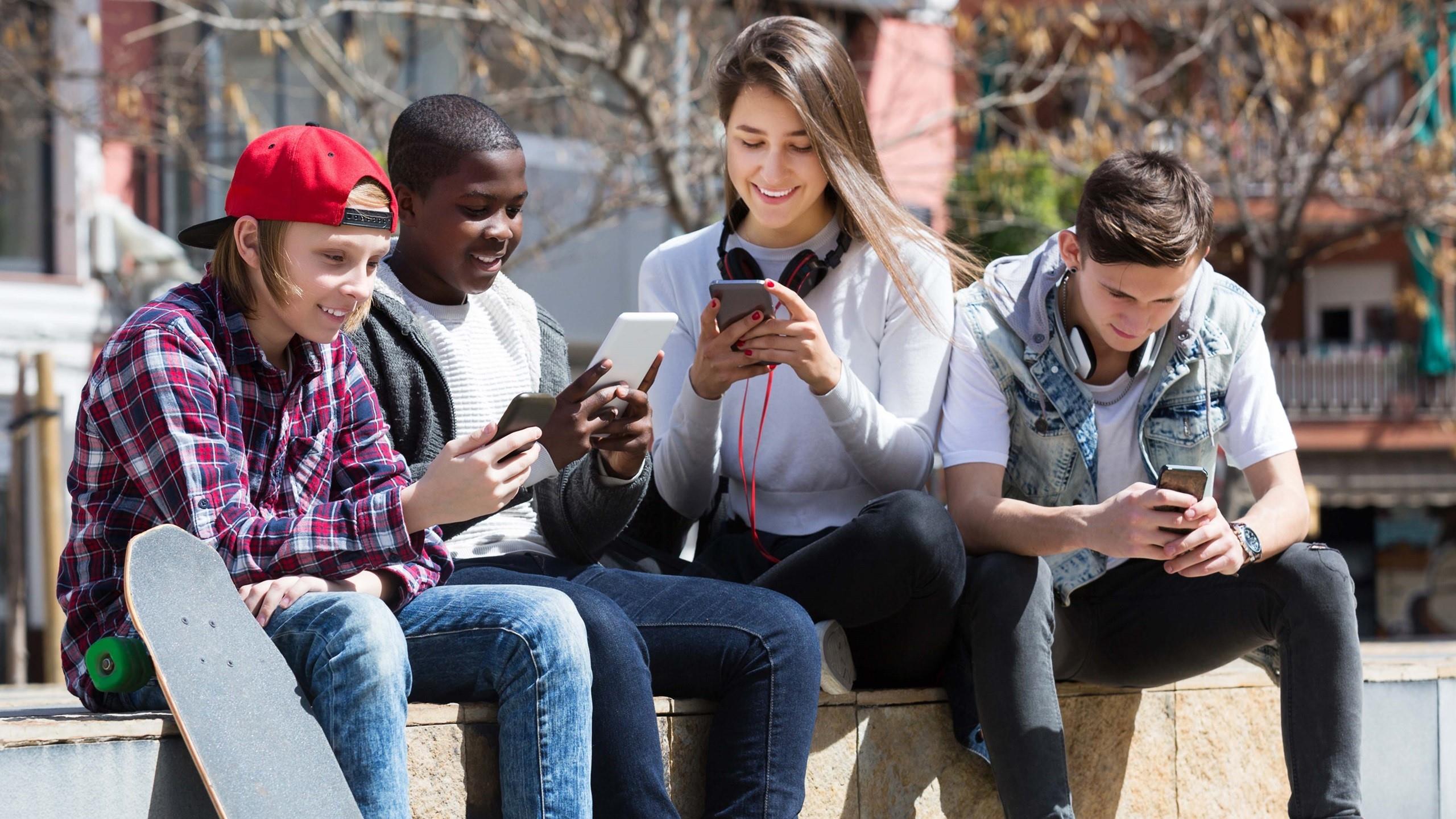 Ungdommer sitter på en benk og ser på hver sin mobil