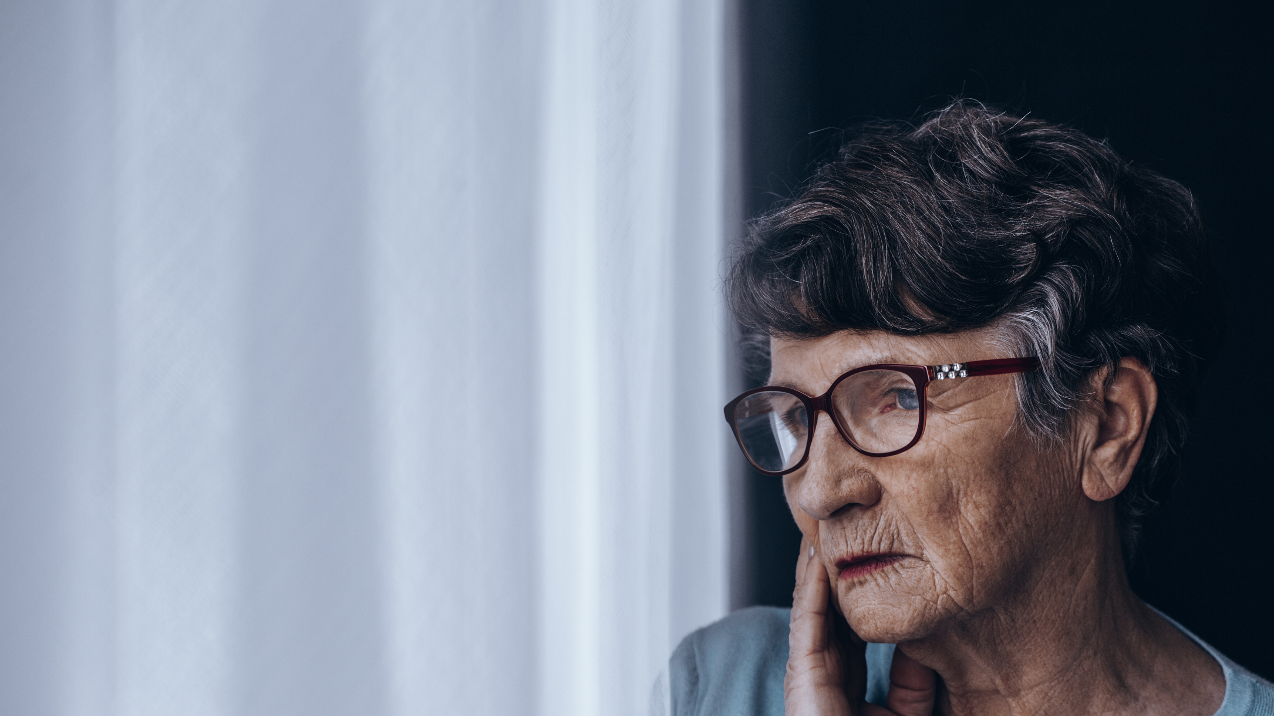 Eldre dame med briller står ved et vindu.