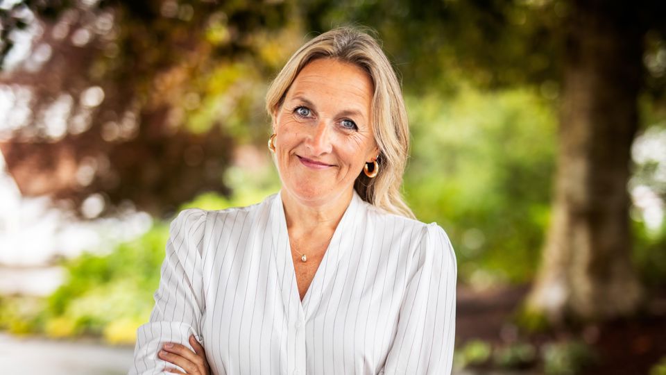 Kvinne med lyst halvlangt hår, og kryssa armar smiler og ser rett i kamera. 