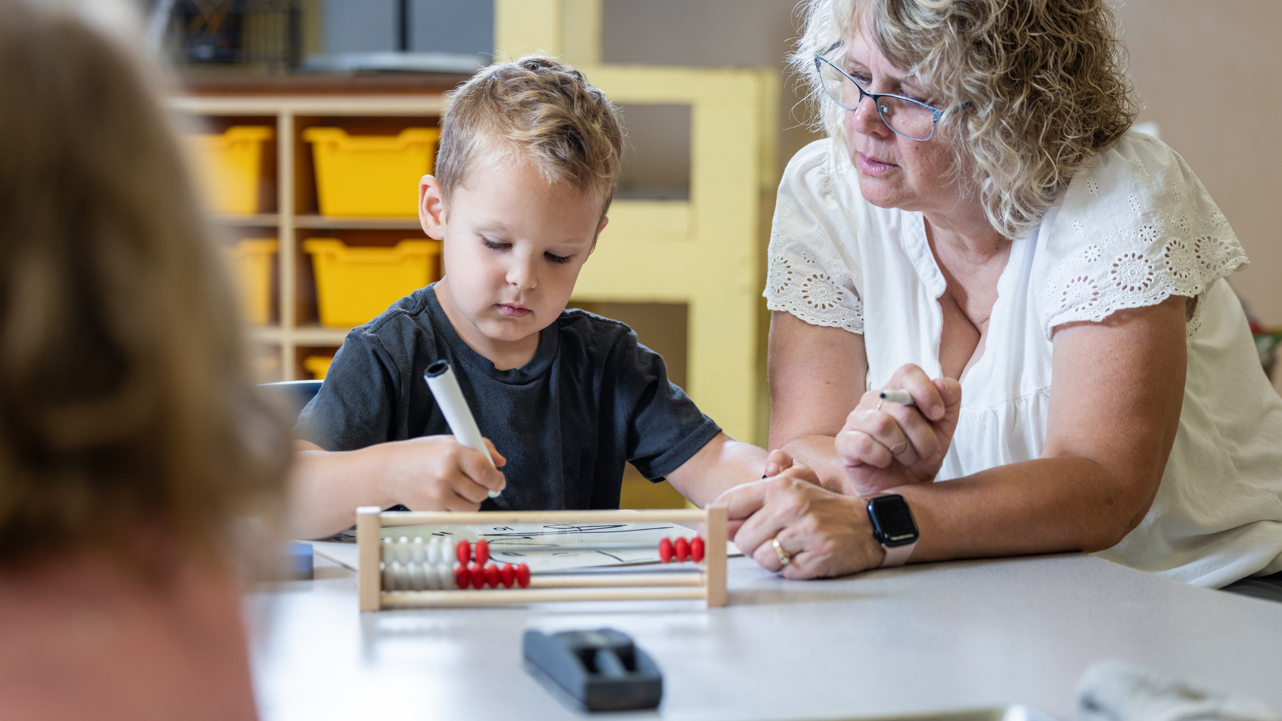 Kvinne sitter ved siden av ung gutt som tegner og ser på en kuleramme. 
