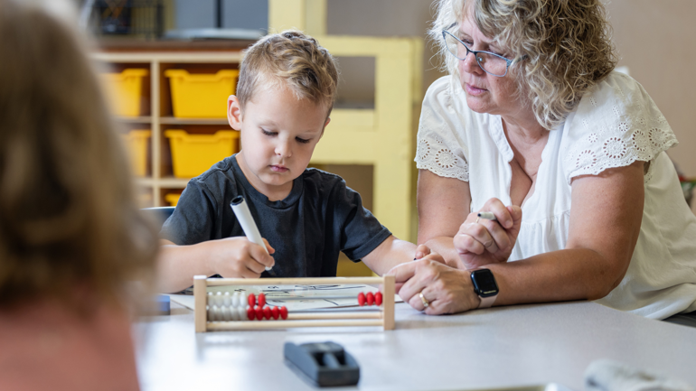 Kvinne sitter ved siden av ung gutt som tegner og ser på en kuleramme.