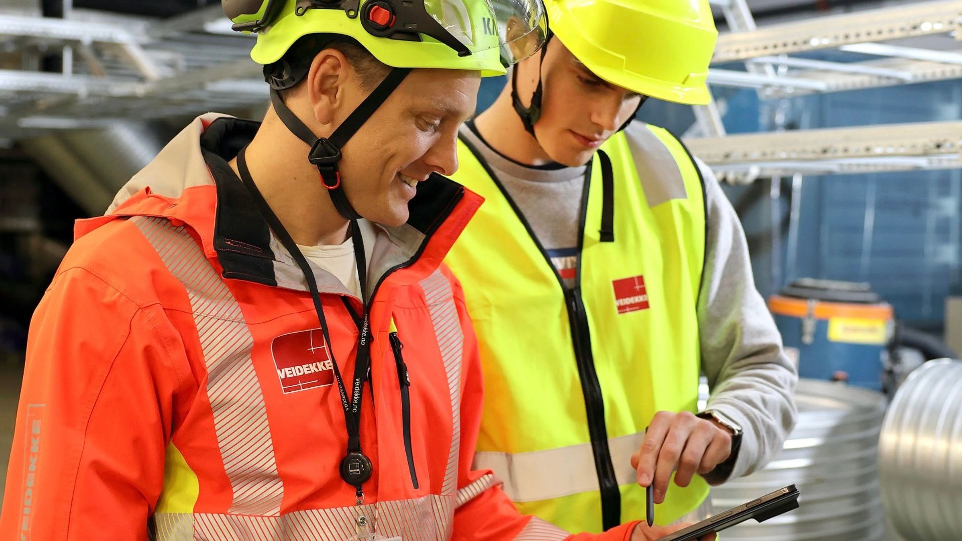 To arbeidstakere på en byggeplass snakker sammen.