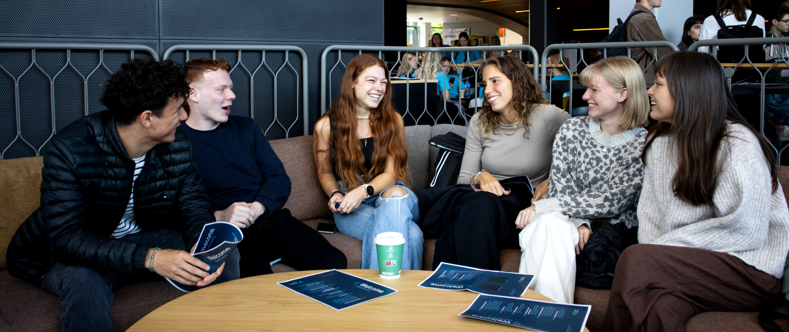 Seks studenter sitter i en sofagruppe i Global Lounge, smiler og ser på hverandre