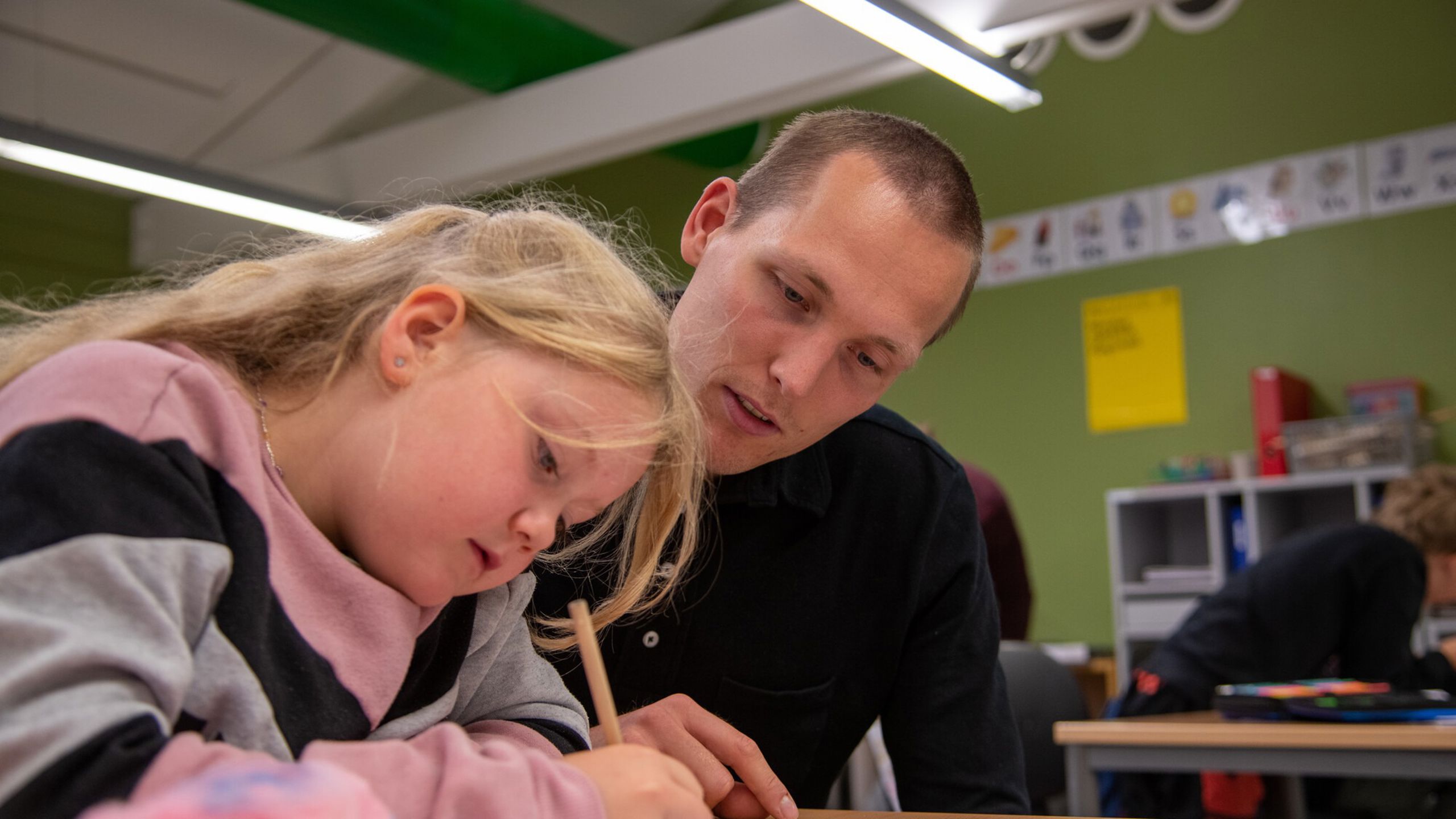 lærer sitter ved siden av elev i barneskolealder og ser på en oppgave