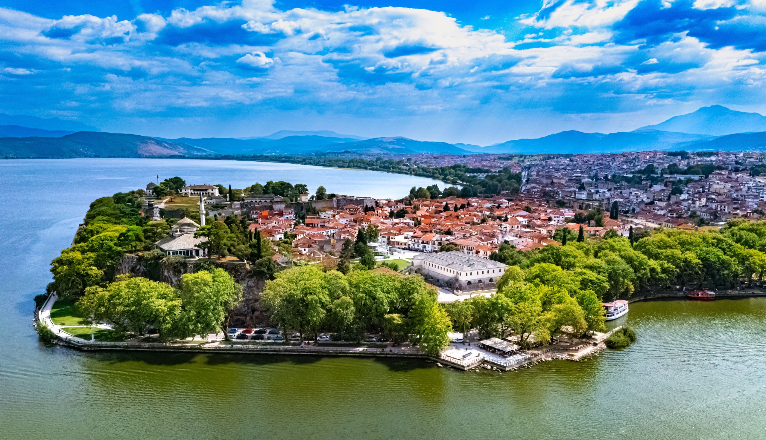 Bilde av byen Ioannina, ytterst langs kystlinjen. Begyggelse med røde tak, og fjellkjede i horisonten.