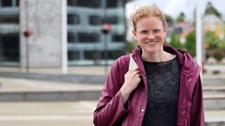 Kvinne står utenfor campus Bergen i regnjakke. Hun smiler. 