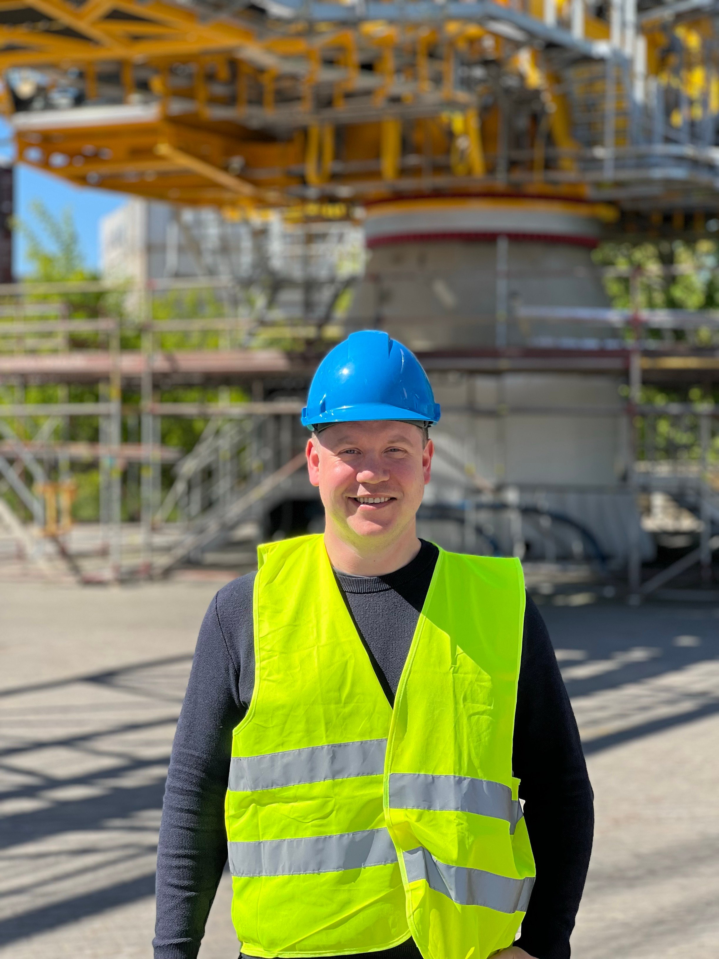 Thorstein Ravneberg Rykkje står smilande framfor ei svær kran. Han har på seg blå arbeidshjelm og gul refleksvest.