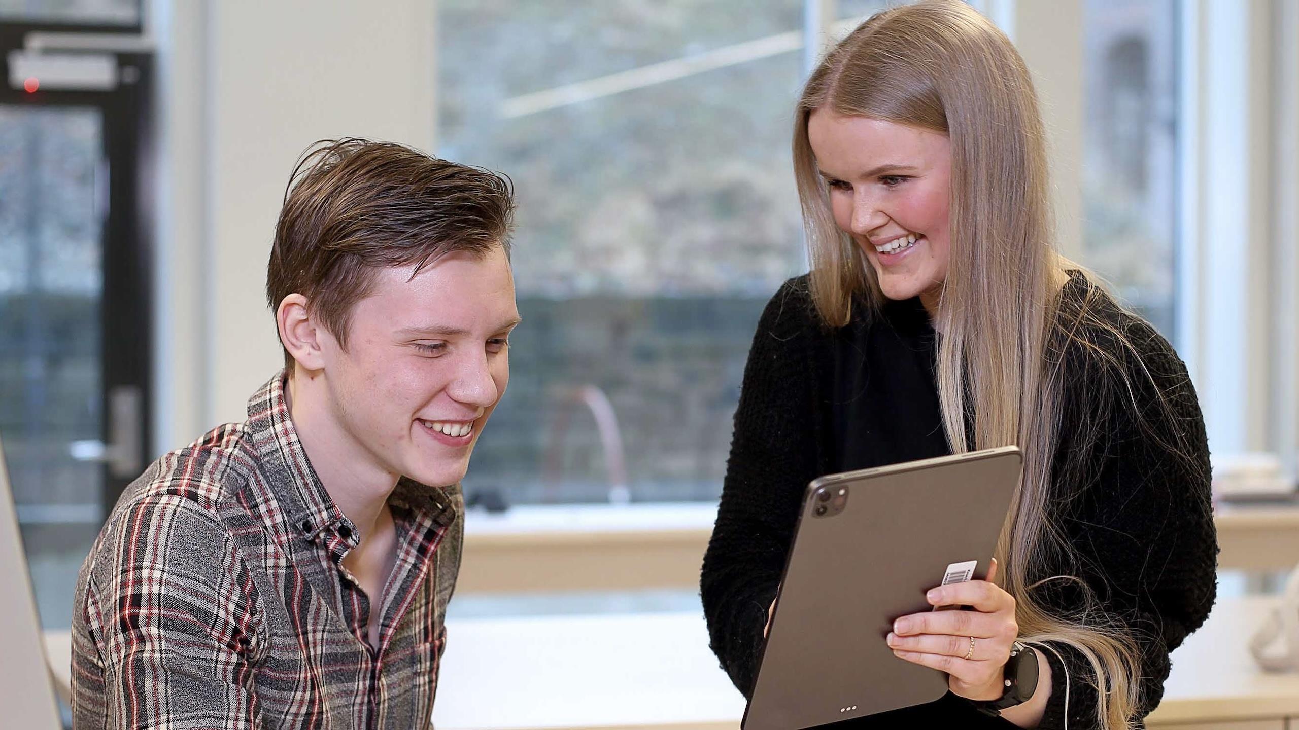 A male and a female student is looking at a tablet.
