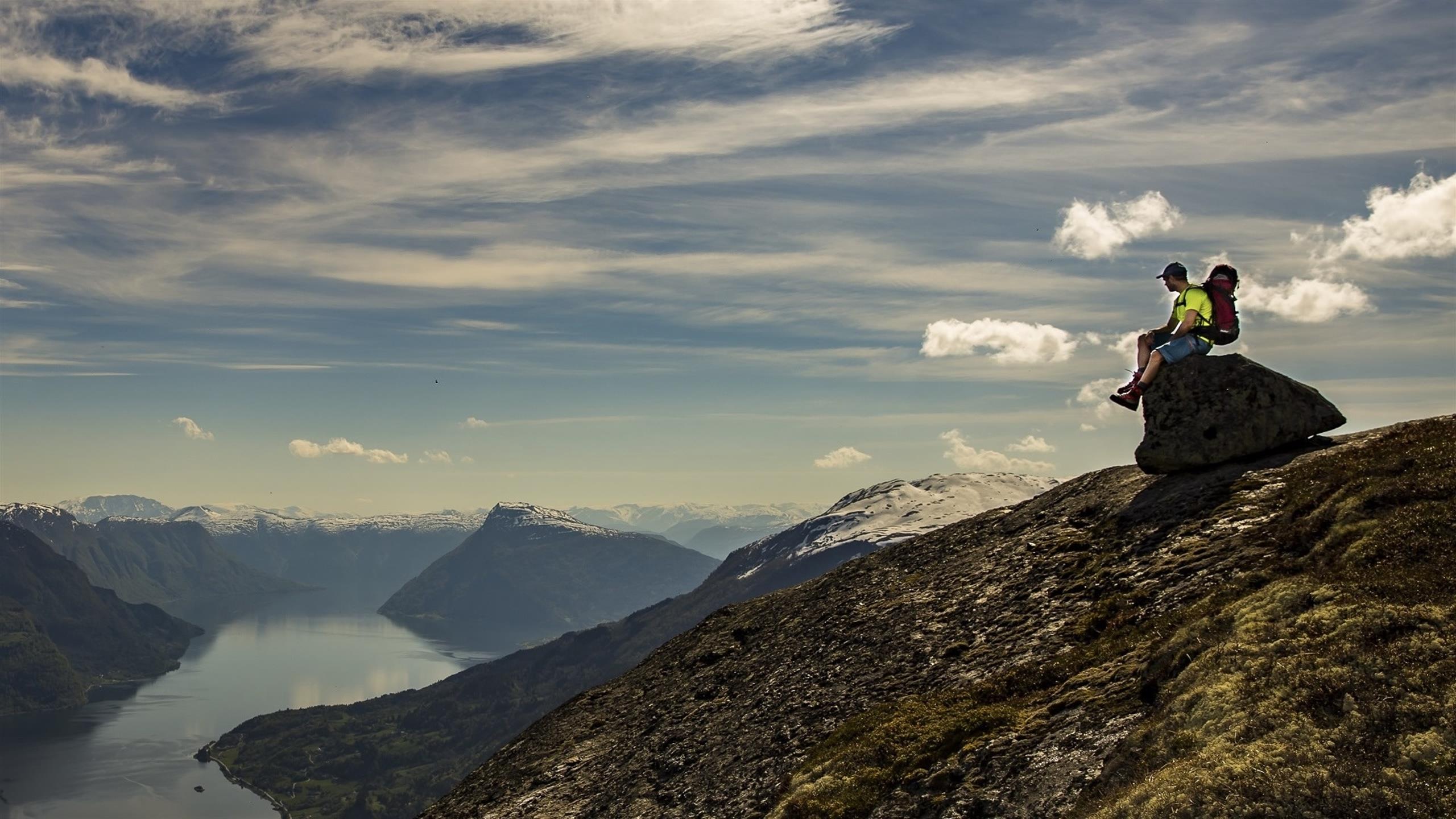 A person sitting on a rock and looking at the view over the fjords and mountains.