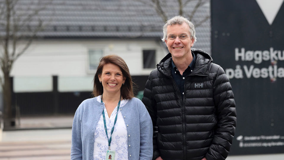 Portrettfoto av to tilsette. Dei står ute framfor HVL-skiltet.