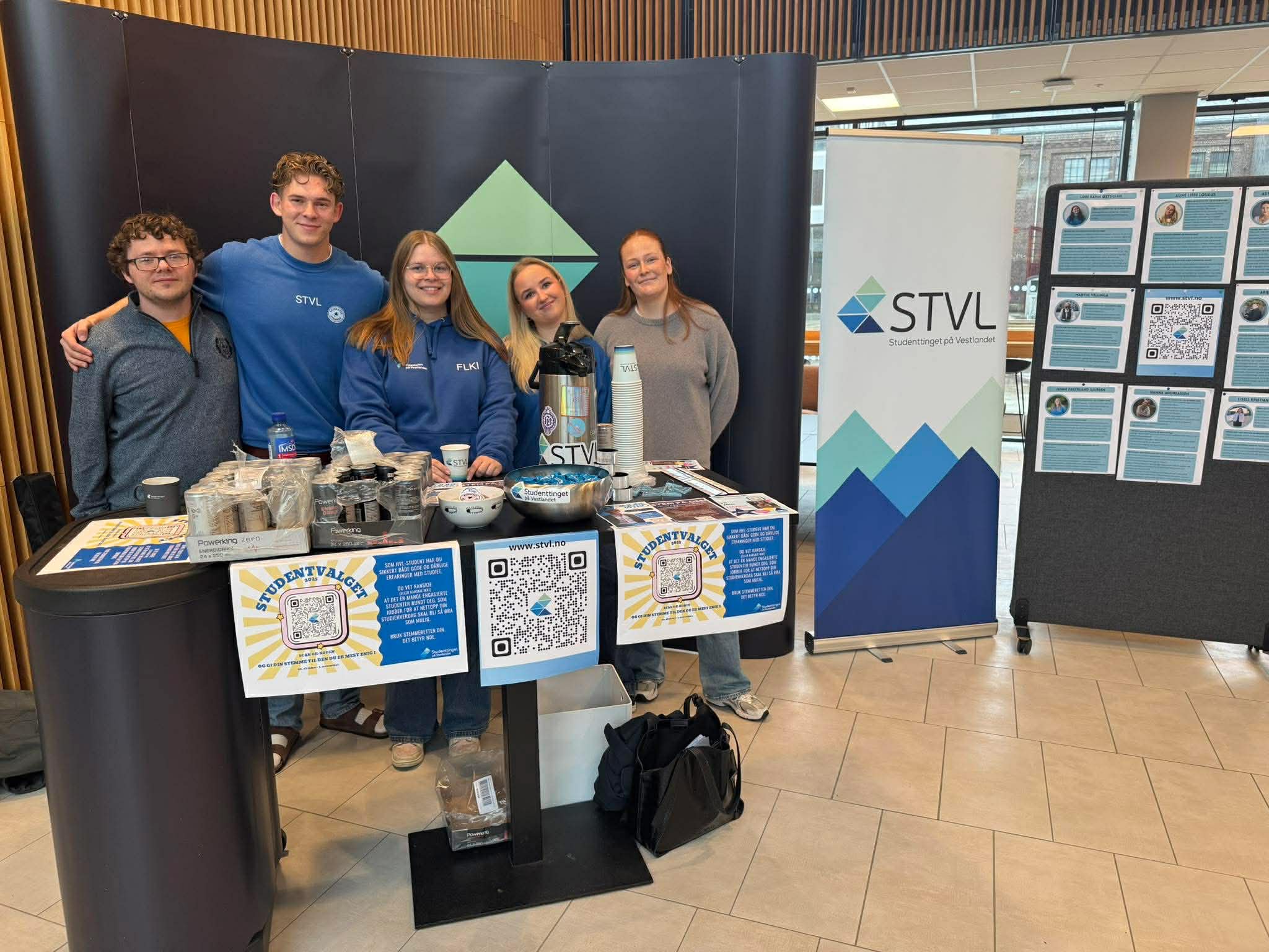 Fem studentar på stand. Messevegg i bakgrunnen.