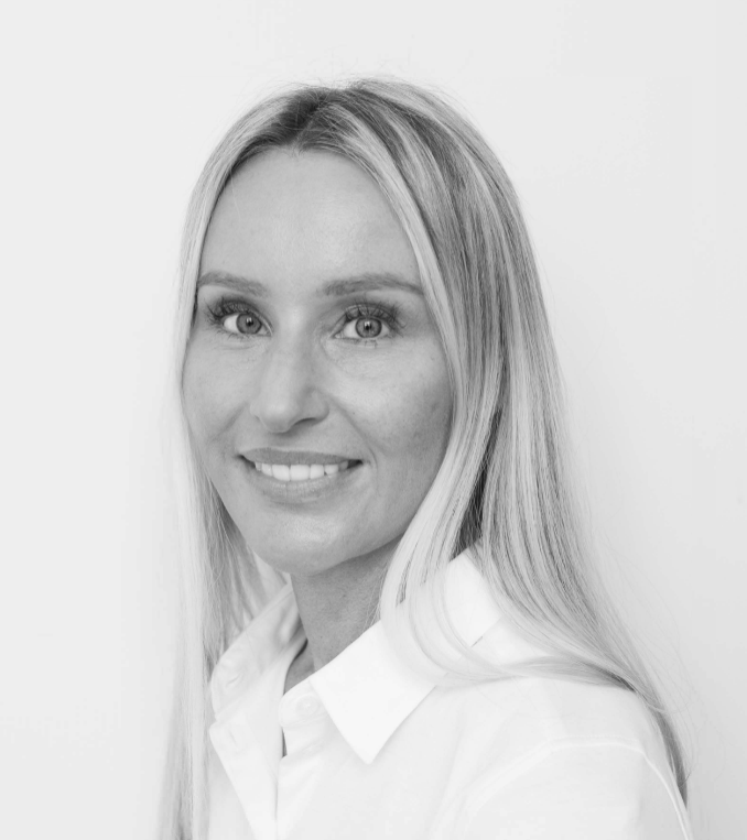 Eit portrettbilde i svart-kvitt av Sigrid Haukanes, ein person med lyst hår, kledd i kvit skjorte. Sigrid ser mot kamera og smiler.