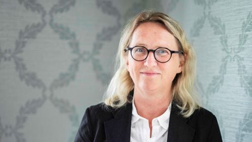 Christine Øye smiler til kameraet. Ho har blondt hår og er kledd i svart blazer og kvit skjorte. I bakgrunnen er ein gammaldags blåaktig tapet med mønster.