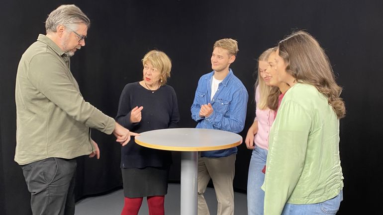 En gruppe mennesker står rundt et bord og snakker sammen.