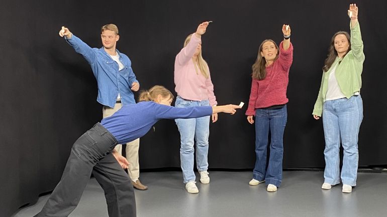 Fem unge mennesker strekker seg med en utstrakt arm, og holder en liten papirlapp mellom fingrene.