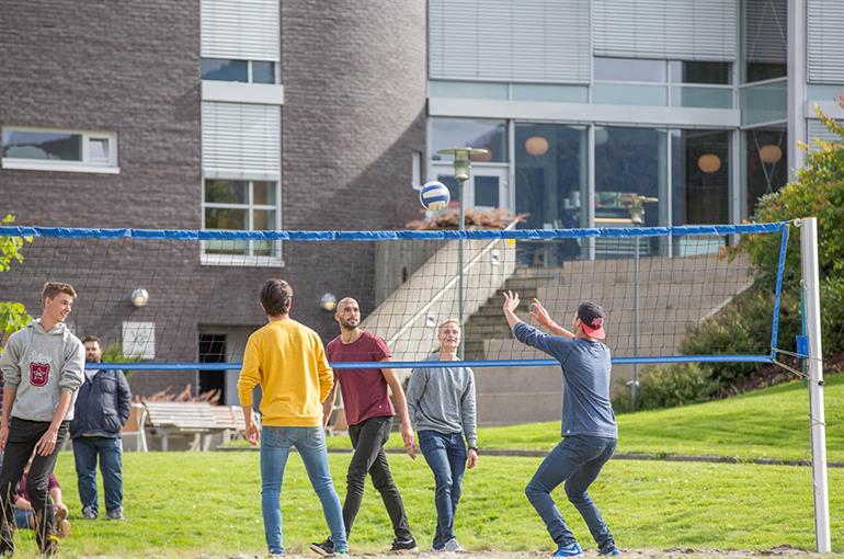 Studentar spelar sandvolleyball utanfor Høgskulebygget. 