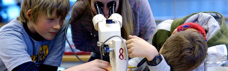 Lærarstudent og elevar brukar mikroskop