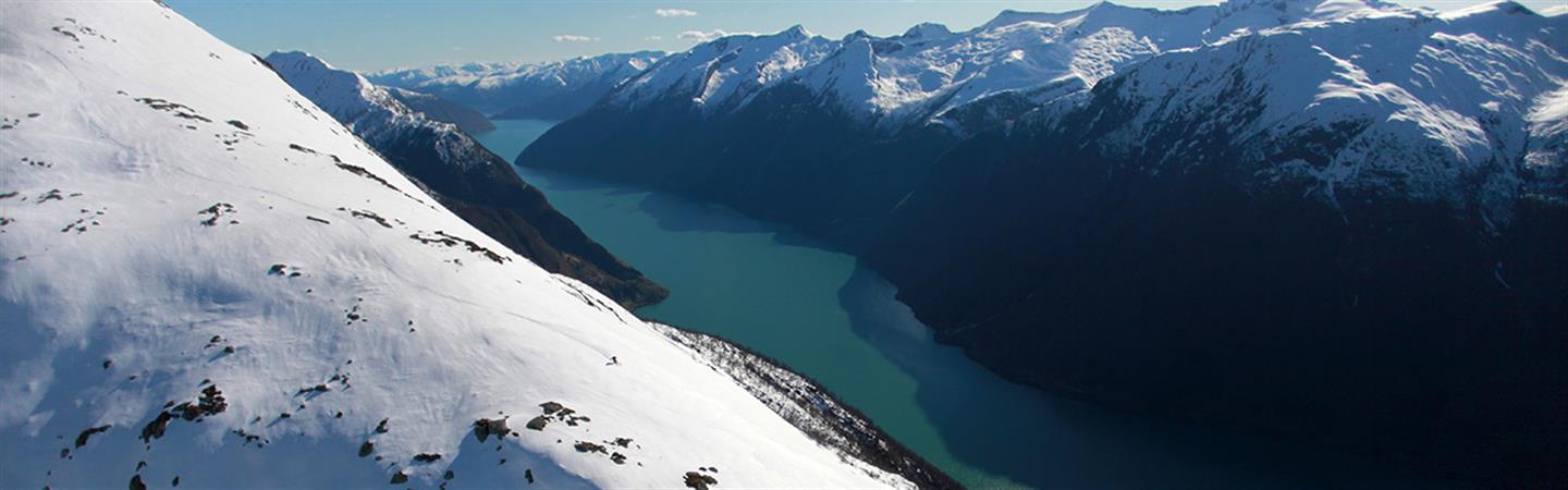 Panoramabilde av snødekte fjell og blå fjord.