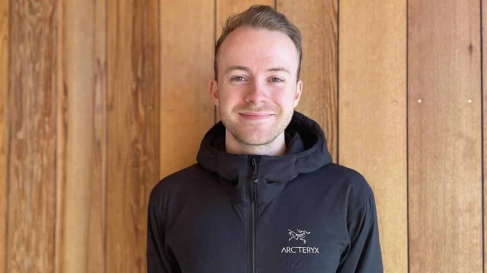 Smilende student står foran en trevegg. 