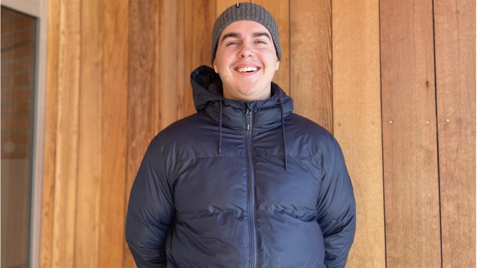 Student poserer foran en trevegg, og ser svært fornøyd ut. 