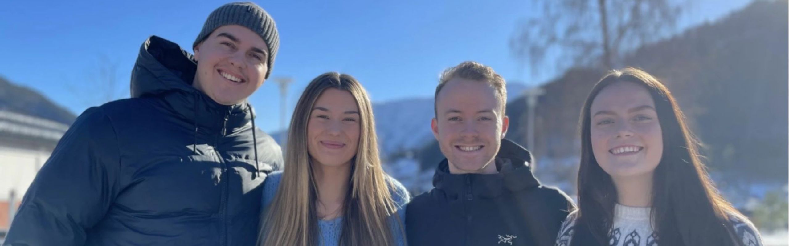 Fire glade studenter smiler til kameraet ute i sola. 