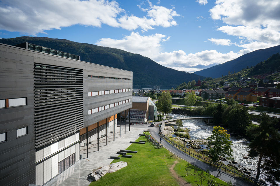 Campus Sogndal med blå himmel, høgskulebygget og elv.