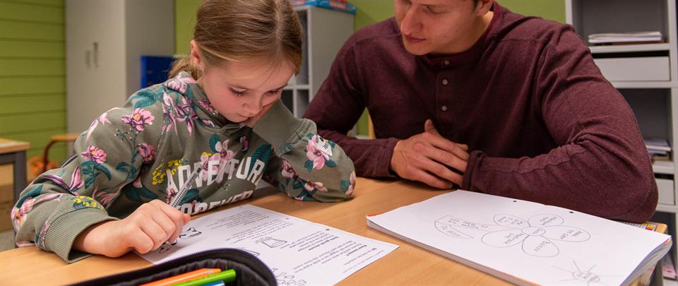 Student i praksis på skole. Sitter sammen med elev i klasserommet. 