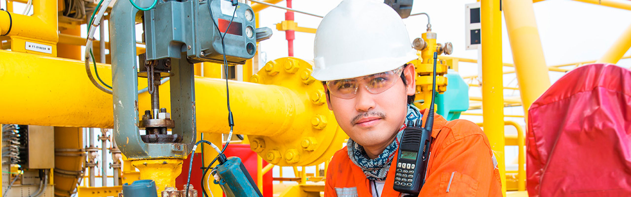 Mann på oljeplattform med hjelm og briller.