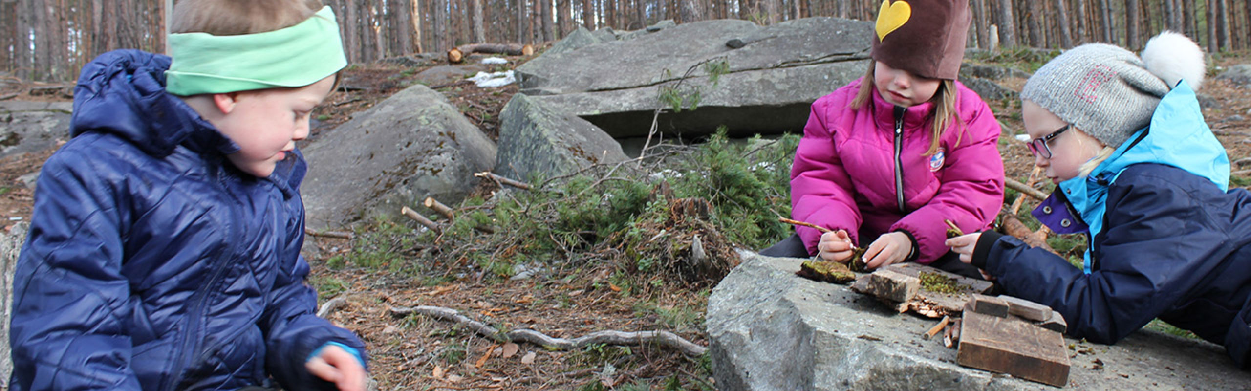Tre barnehageungar leikar ute i skogen.