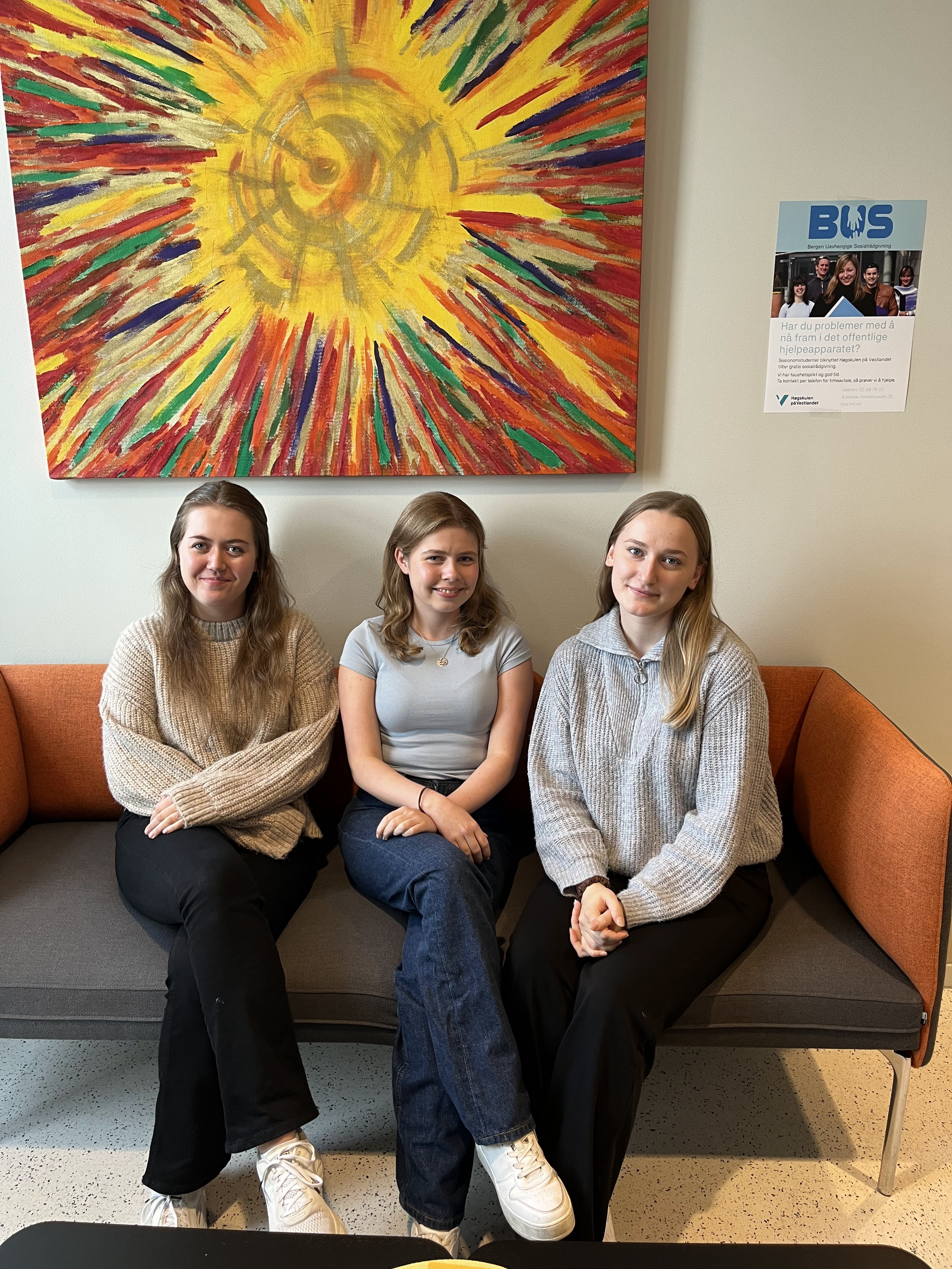 Tre unge mennesker i en sofa, og et stort maleri på veggen bak dem.