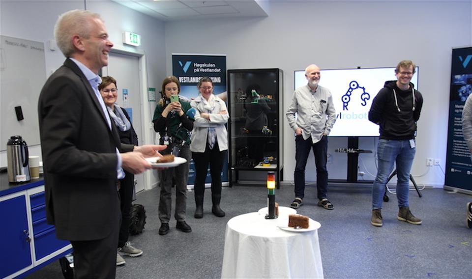 Robotbordet kjører opp til en mann (Roy Stian Farsund fra Sparebanken Sogn og Fjordane), og han ler. I bakgrunnen står andre personer og ser på, og smiler også av robotbordet som serverer kake til bankdirektøren.