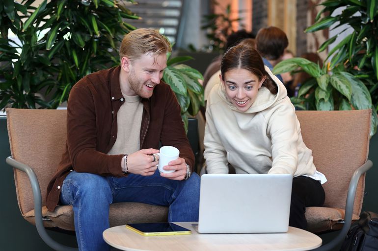 To unge som sitter foran en pc-skjerm i kantinen.