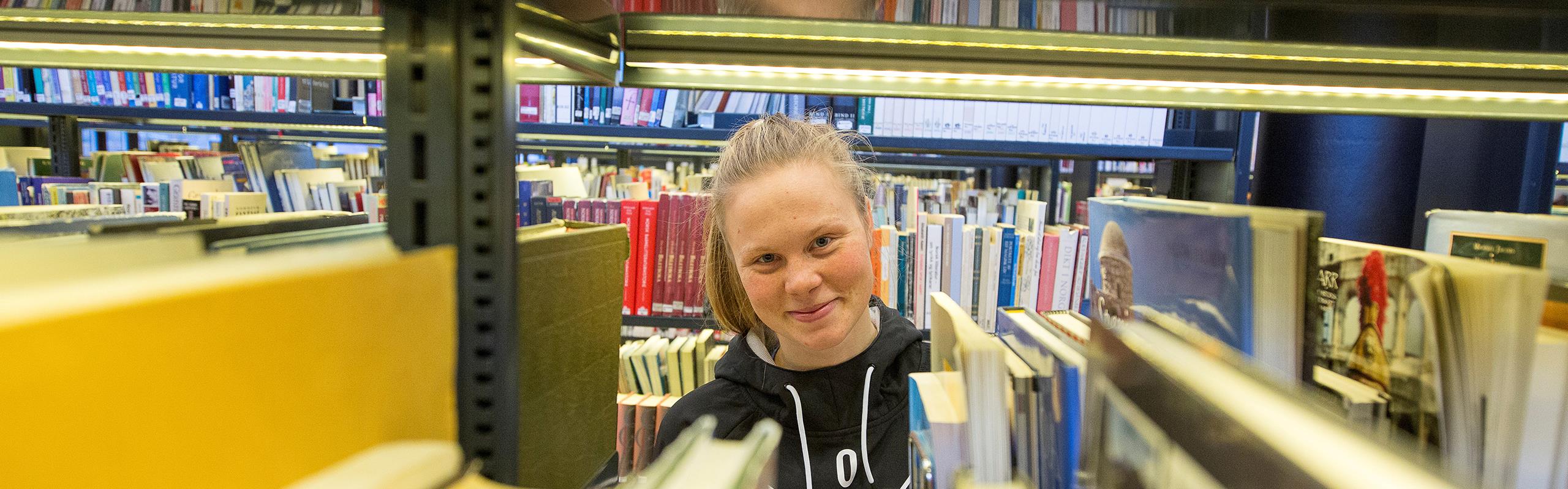 Kvinneleg student ved bokhyller på biblioteket.