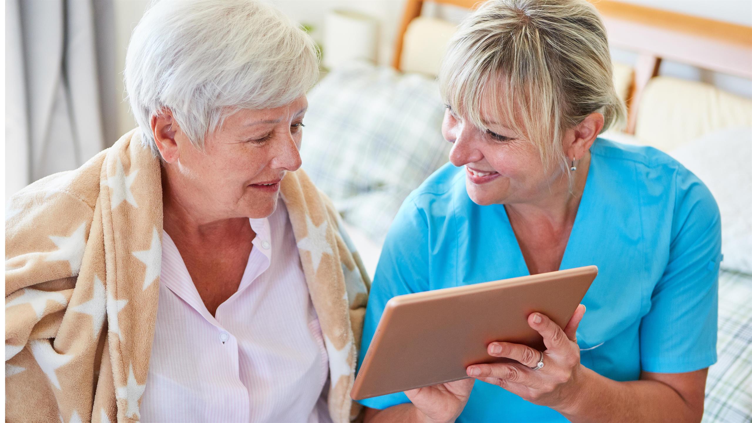 En kvinnelig helsearbeider viser en eldre kvinne noe på en skjerm. 