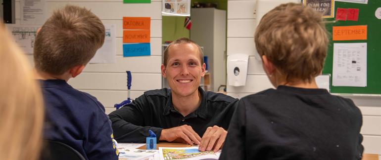 A smiling young man looking into the camera and helping to kids.