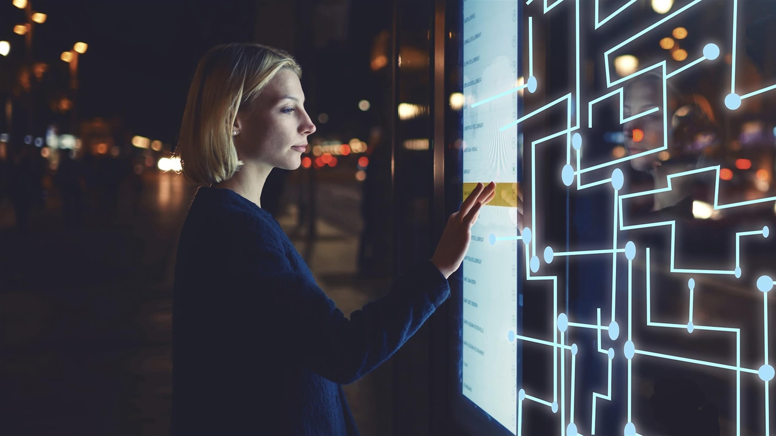 En kvinne som trykker på en stor digital skjerm utendørs på kveldstid.