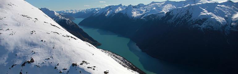 Panoramabilde av snødekte fjell og blå fjord.
